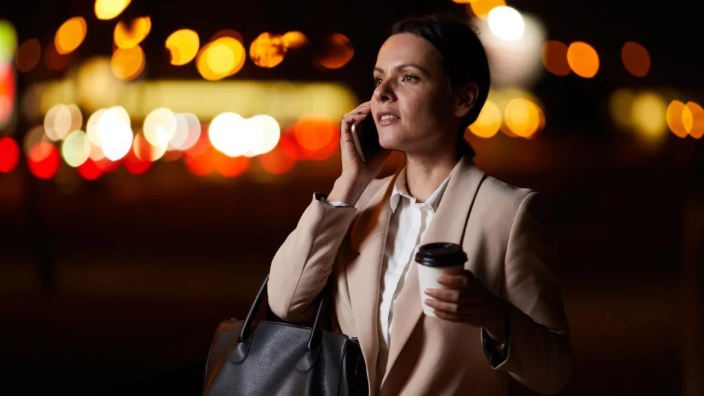 Middle Aged Business Woman With Coffee Outside At Night On Phone.webp 1024x576