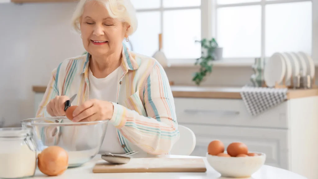 senior woman breaking egg in kitchen.webp.webp